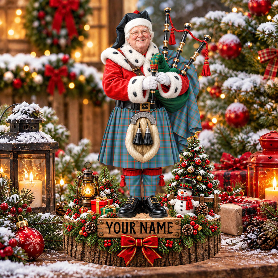 Personalized Christmas piper plaque in the Agnew Ancient tartan, standing on a snowy log base with a name plaque