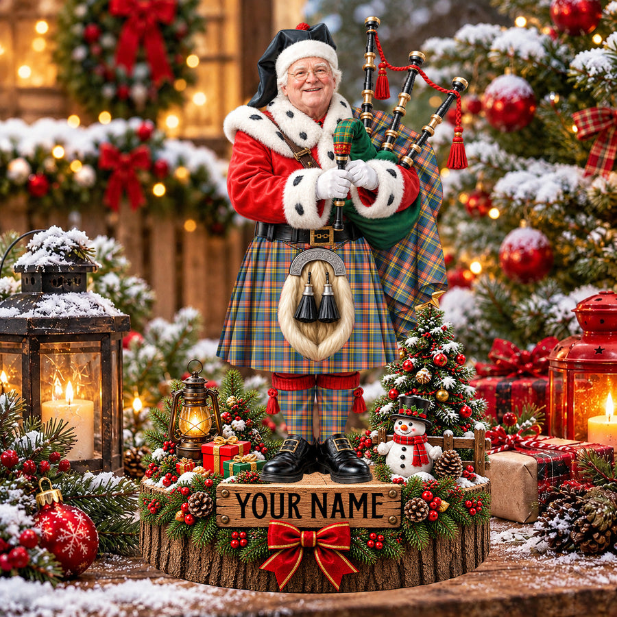 Personalized Christmas piper plaque in the Buchanan Ancient tartan, standing on a snowy log base with a name plaque