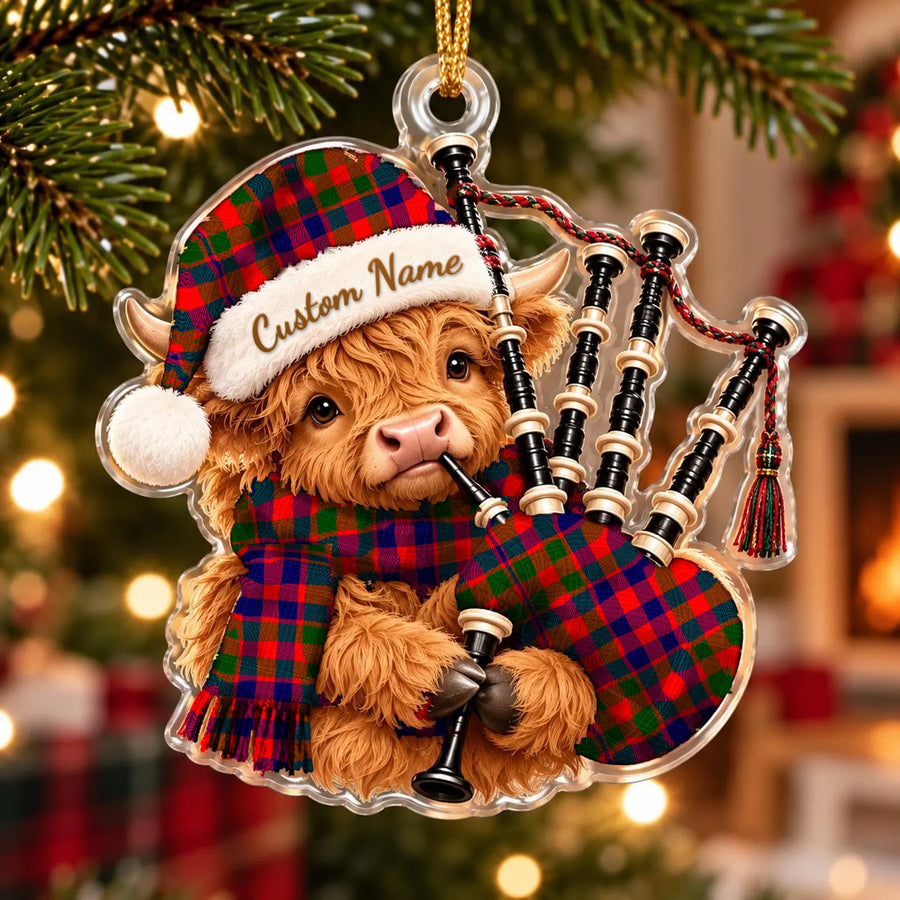 Acrylic Highland cow calf ornament playing the bagpipes, in a Gow Modern tartan Santa hat, scarf and pipe bag, with a custom name on the hat