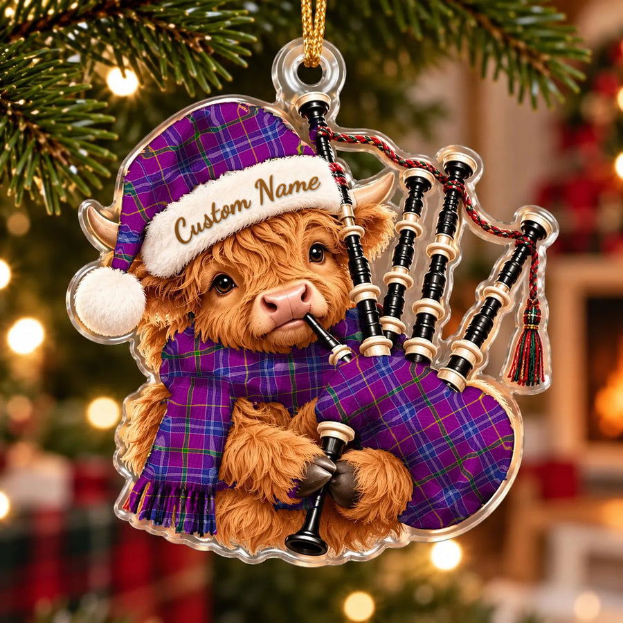 Acrylic Highland cow calf ornament playing the bagpipes, in a Jackson tartan Santa hat, scarf and pipe bag, with a custom name on the hat