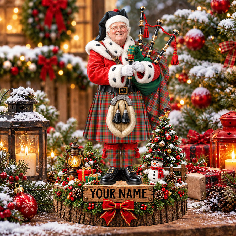 Personalized Christmas piper plaque in the MacPherson Weathered tartan, standing on a snowy log base with a name plaque