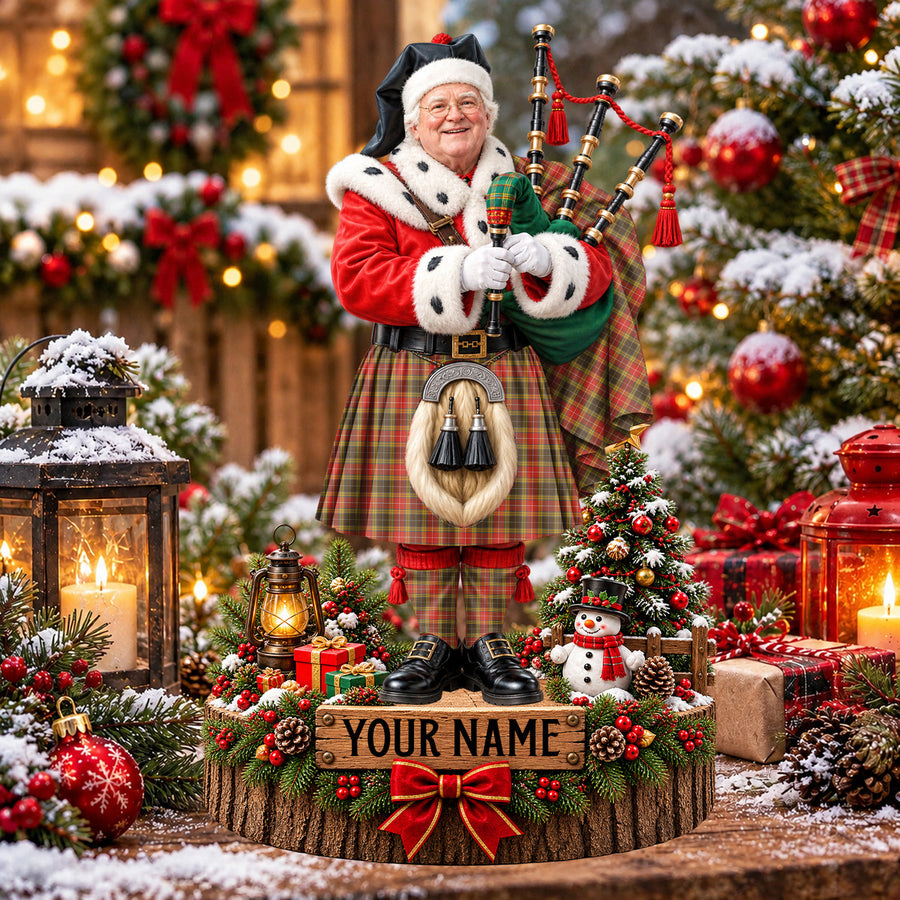 Personalized Christmas piper plaque in the Buchanan Old Set Weathered tartan, standing on a snowy log base with a name plaque