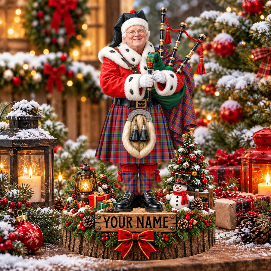 Personalized Christmas piper plaque in the Cameron of Lochiel tartan, standing on a snowy log base with a name plaque