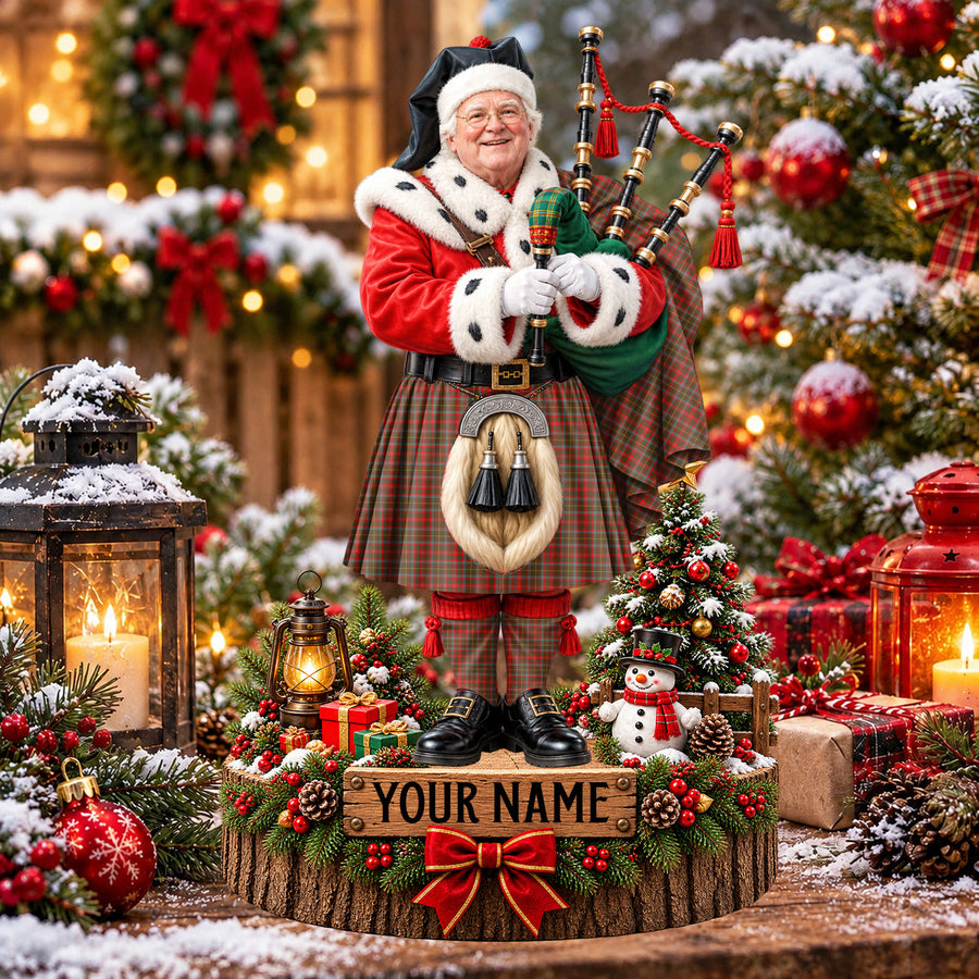 Personalized Christmas piper plaque in the MacKintosh Hunting Weathered tartan, standing on a snowy log base with a name plaque